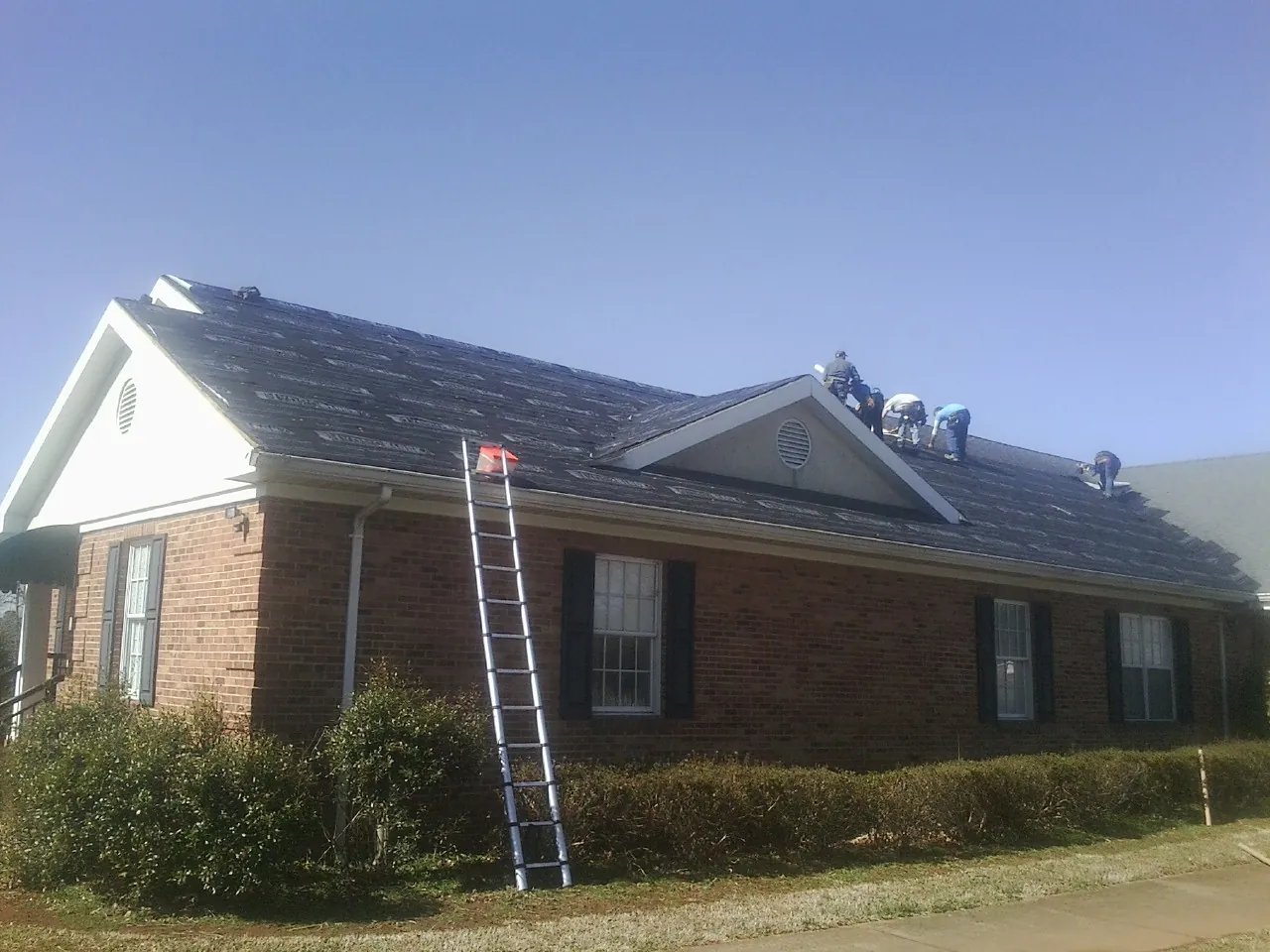 Crew tearing shingles off a brick ranch roof with a ladder set — Emergency Roof Repair work by our crew in Tyrone