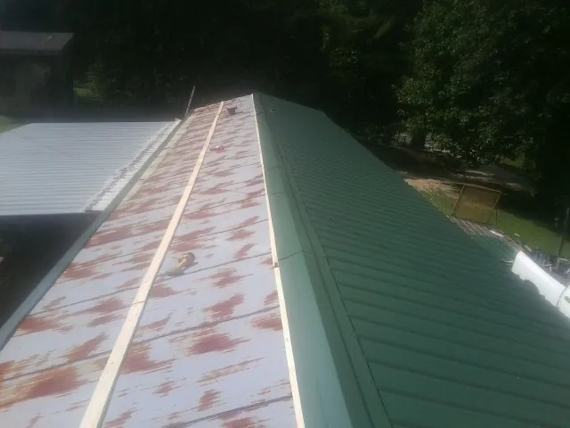 Old rusted panels beside newly installed green metal roofing — Wind Damage Roof Repair by Roofing Brothers in Tyrone