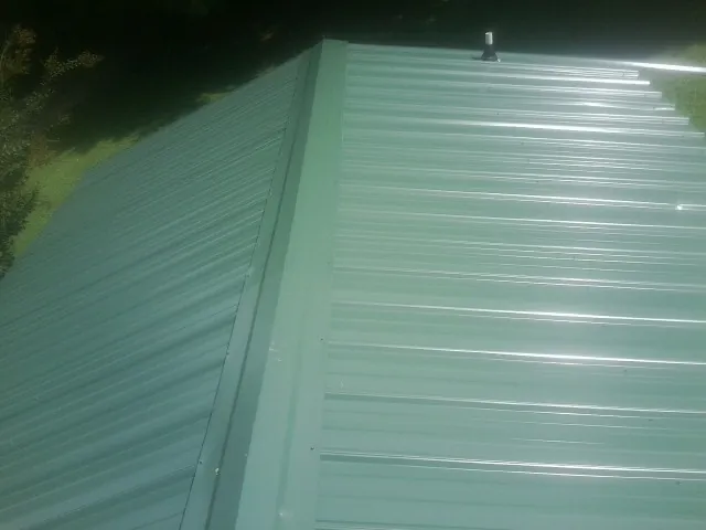 New green metal panels meeting at the ridge of a roof — Flat Roof Repair work by our crew in Tyrone